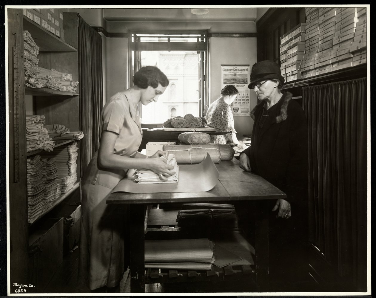 Young woman wrapping up cloth materials for a home worker to take with her, at the New York Association for the Blind, 111 East 59th Street, New York by Byron Company