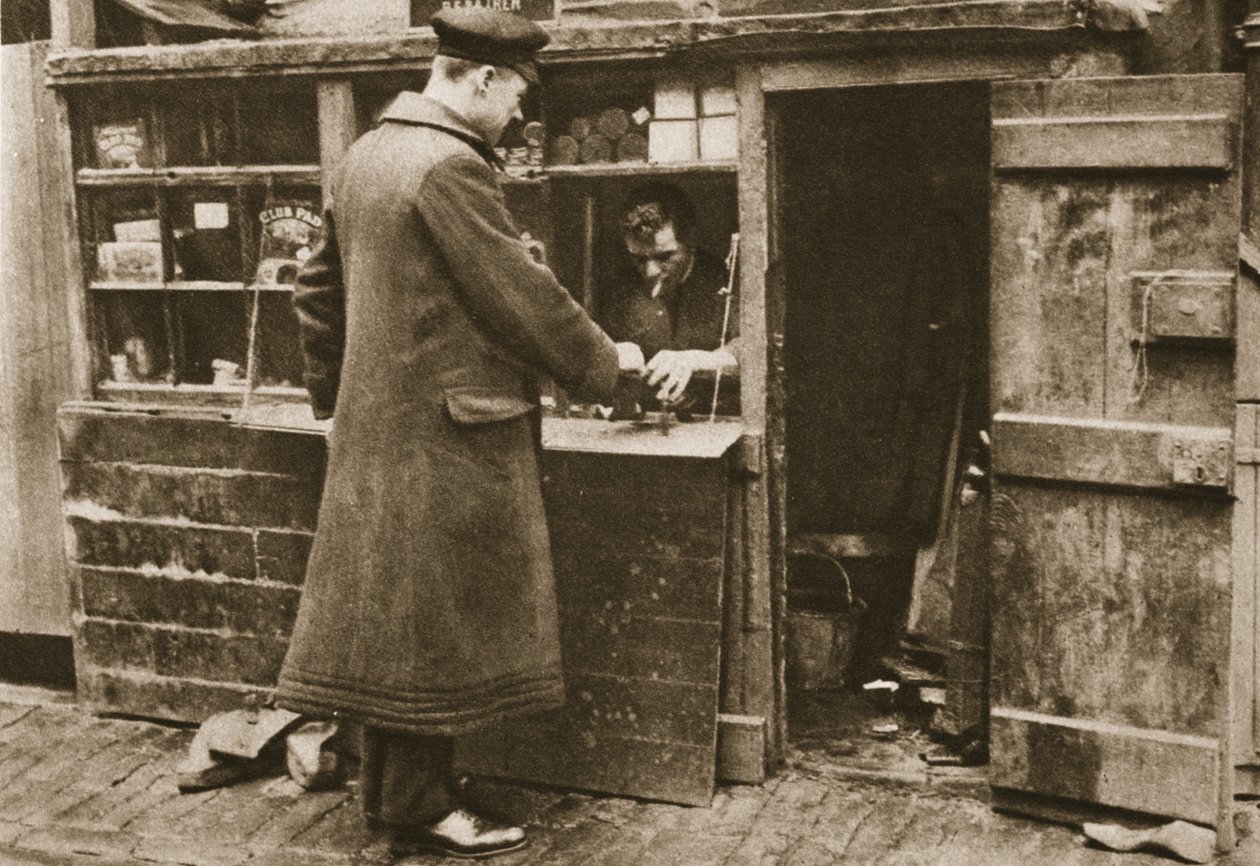 A cobbler, established in a makeshift booth in a cobbled Mayfair mews, takes in boots from a chauffeur, from Wonderful London, published 1926-27 by English Photographer