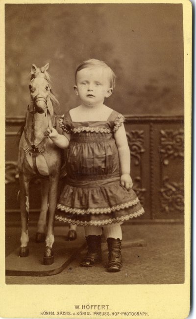 Young girl standing by rocking horse by W. Hoffert